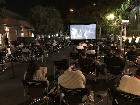 People seated in lawn chairs outside watching a movie