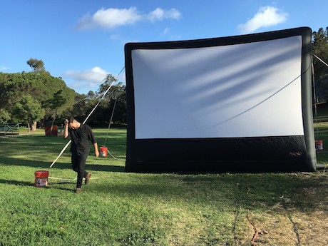 technician setting up outdoor movie screen on grass