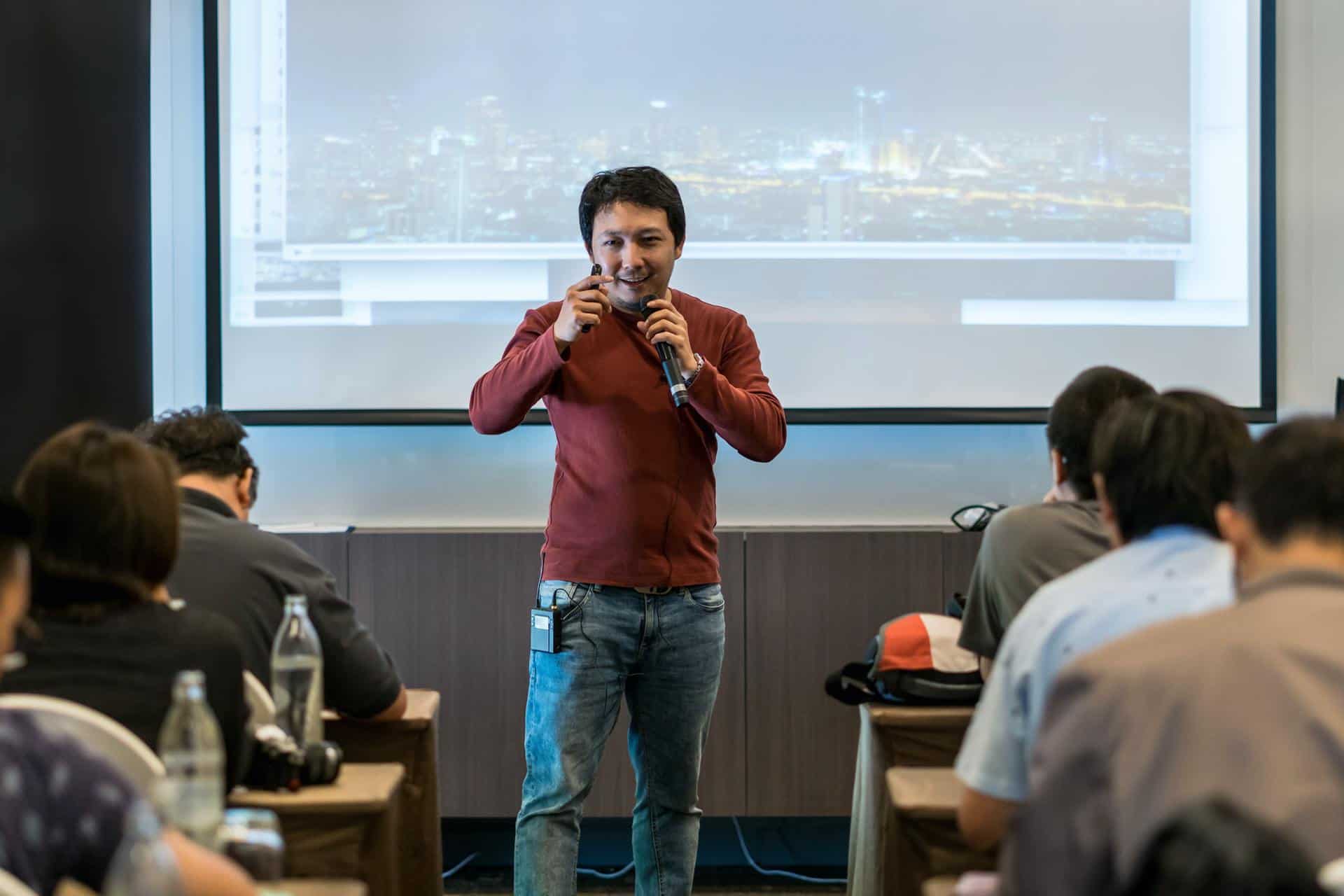 Asian Speaker with casual suit on the stage over the presentation screen in the business