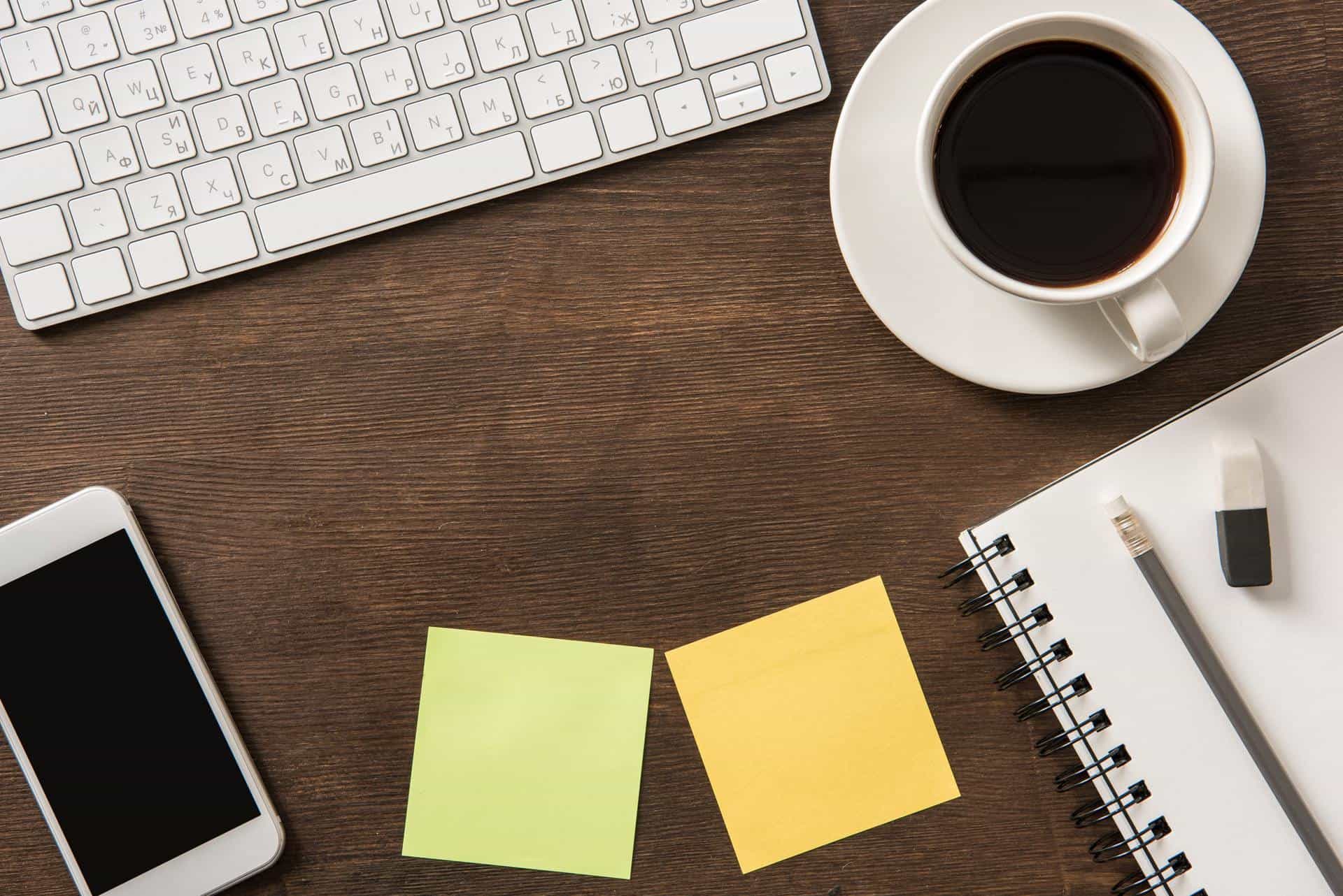 Close-up view of smartphone with blank screen, keyboard, blank notes and cup of coffee at workplace,